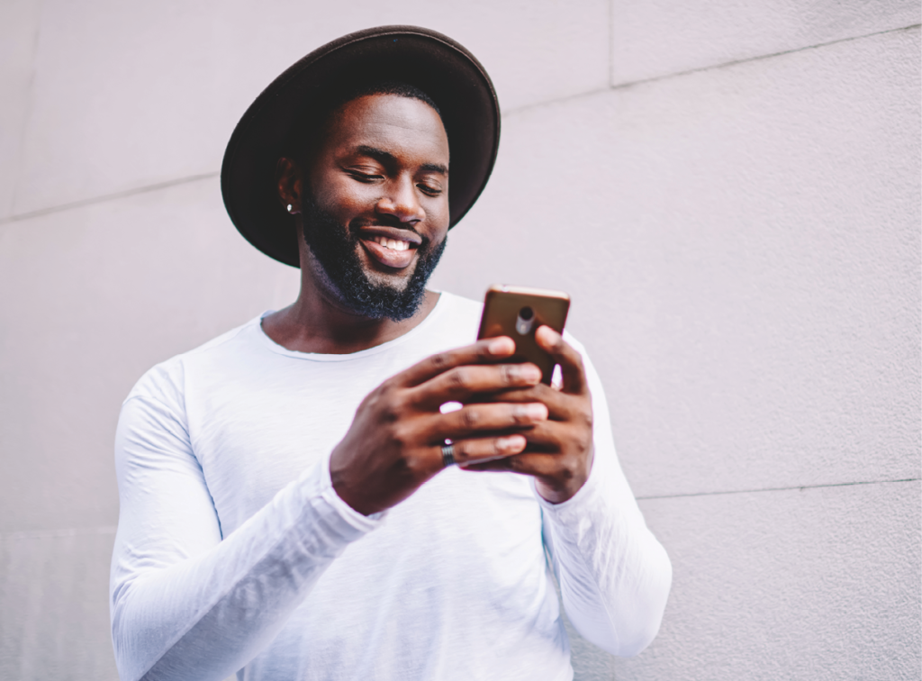 Cheerful guy in stylish wear viewing photos on mobile phone