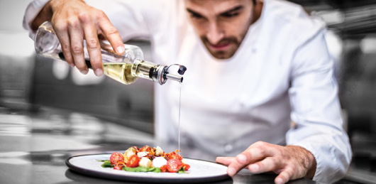 chef pouring olive oil on meal in a commercial kitchen