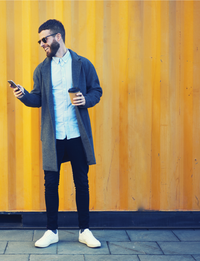 Man walking to work with cup of coffee using modern smartphone