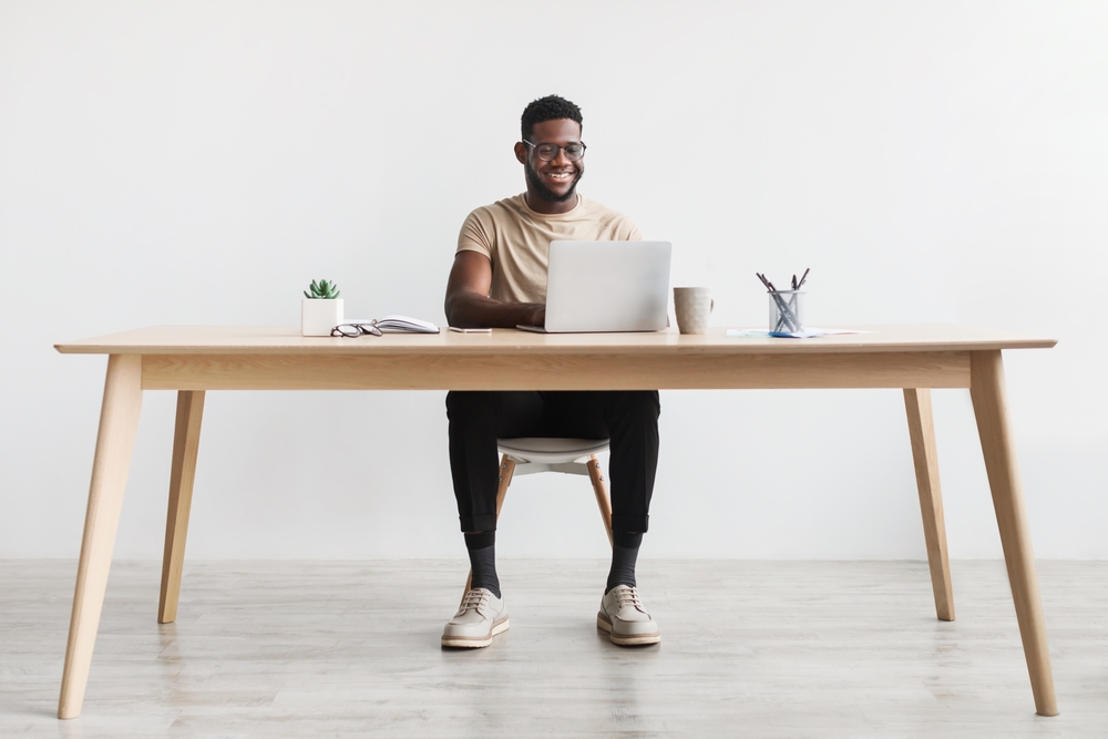 Happy young black man using laptop computer for online work at table in home office